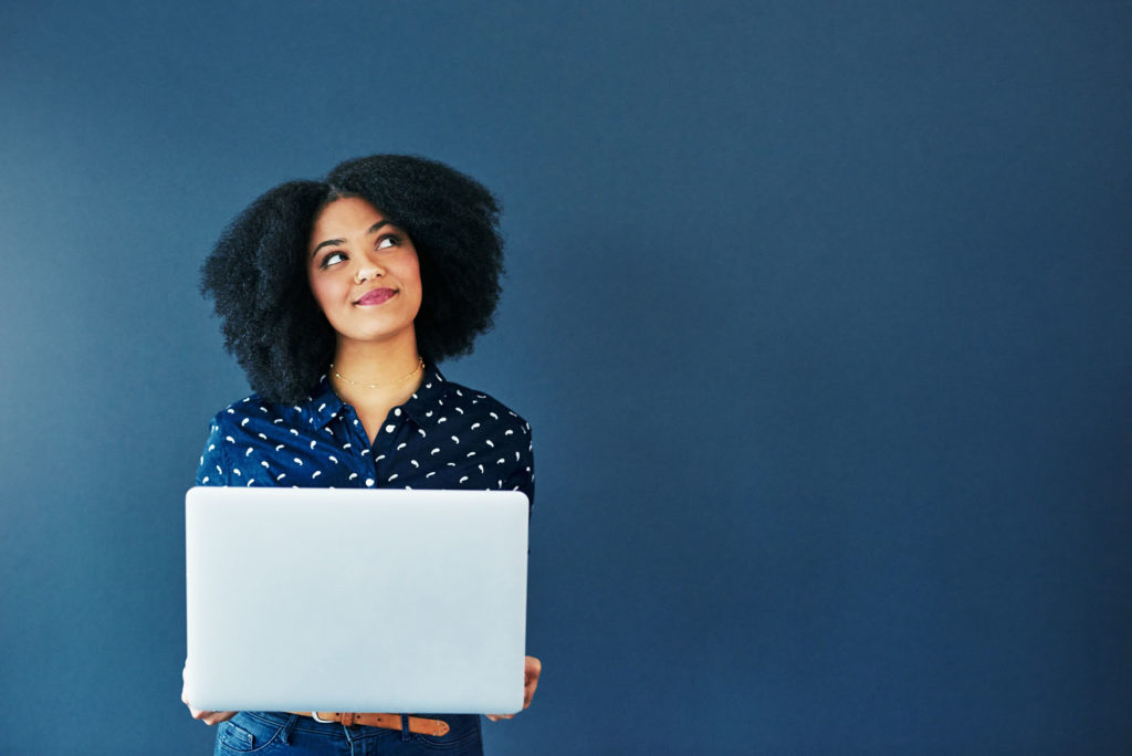 Studio shot of an attractive young woman looking thoughtful while using a laptop against a blue background