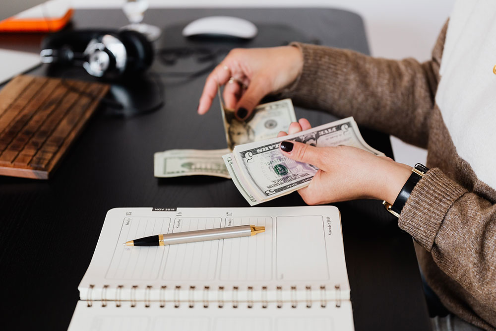Lady's hands holding money on desk near planner