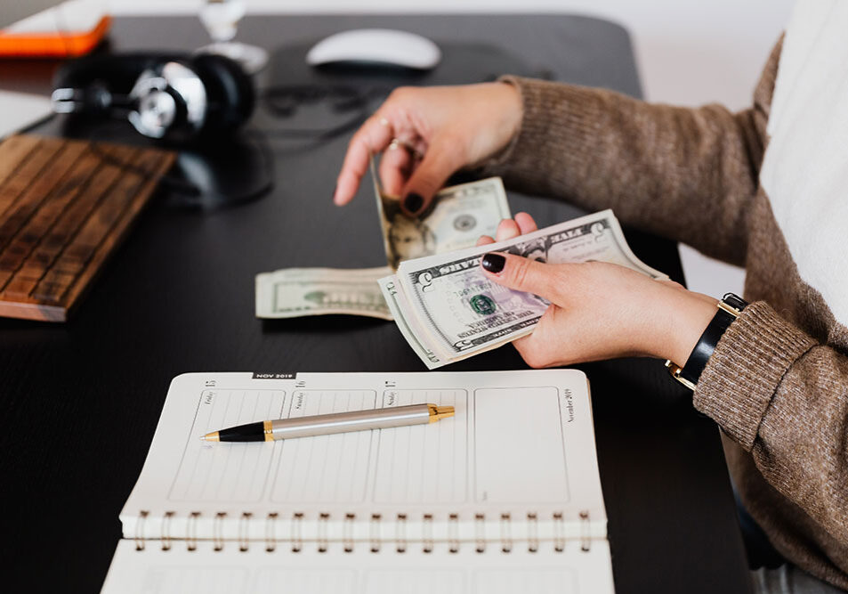 Lady's hands holding money on desk near planner