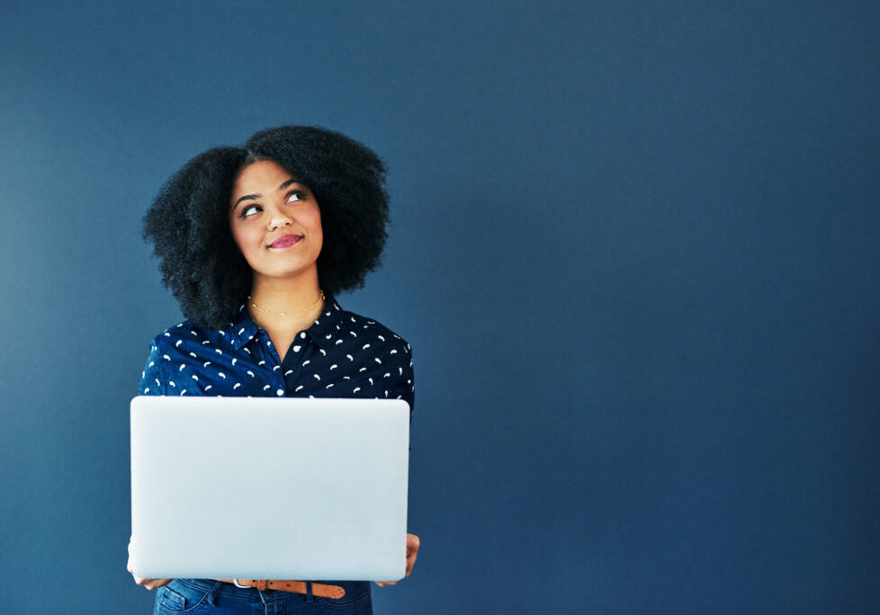 Studio shot of an attractive young woman looking thoughtful while using a laptop against a blue background